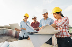 Four people looking at blue prints wearing hardhats | SAE Inc.